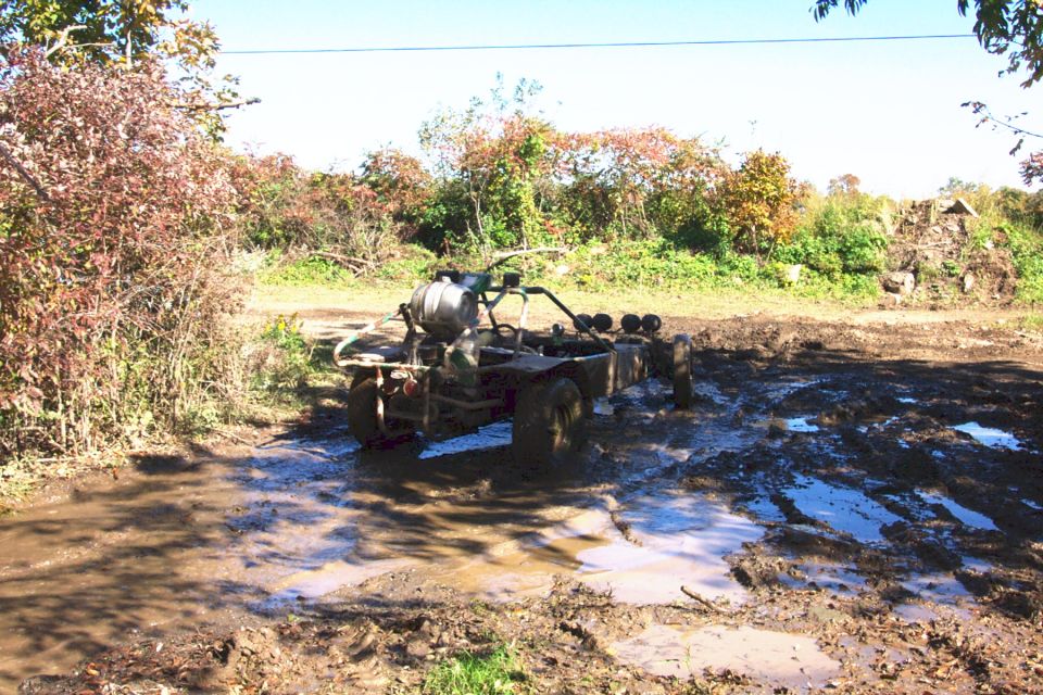 Off-road buggy with a large tank on the back stuck in mud, with four auxiliary lights on the front