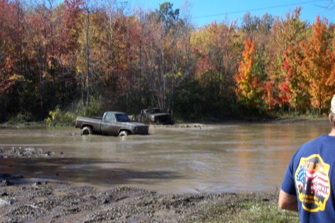 1979 Ford Bronco - Two trucks are stuck in a muddy body of water during autumn.