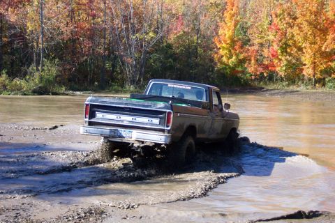 1979 Ford Bronco - Ford pickup truck navigates a muddy terrain during autumn.