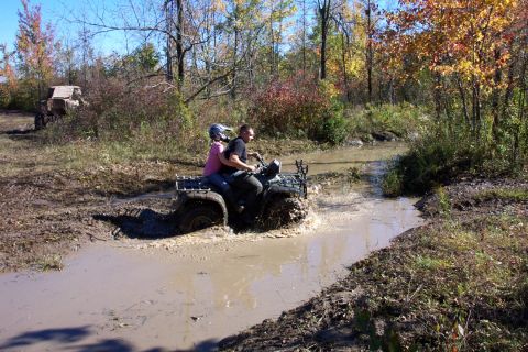 1979 Ford Bronco - Two people ride an ATV through a muddy trail surrounded by autumn foliage.