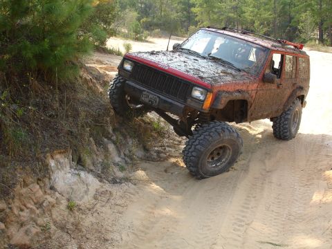 1989 Ford Bronco - Jeep Cherokee XJ navigating a challenging off-road trail with significant mud coverage.