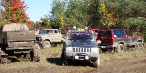 1979 Ford Bronco - Multiple off-road vehicles are stuck in the mud on a sunny day with fall foliage visible.