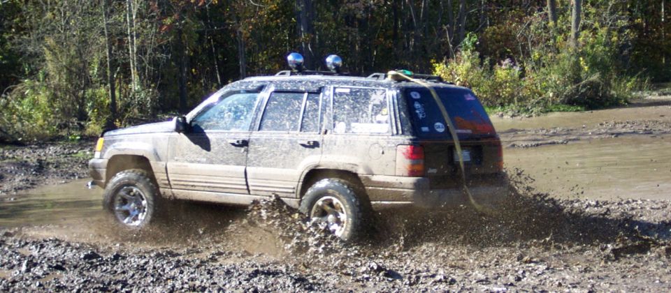 Muddy Jeep Grand Cherokee driving through a water-filled ditch