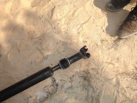 1989 Ford Bronco - A damaged driveshaft lies on the sand, with two people's boots nearby.