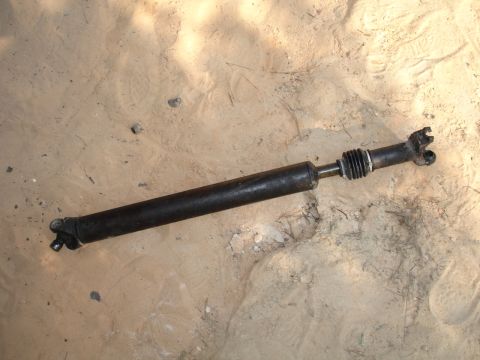 1989 Ford Bronco - A driveshaft with U-joints and a rubber boot is shown lying on a sandy surface.