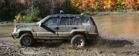 1979 Ford Bronco - Muddy Jeep Grand Cherokee navigates a water obstacle during an off-road excursion.