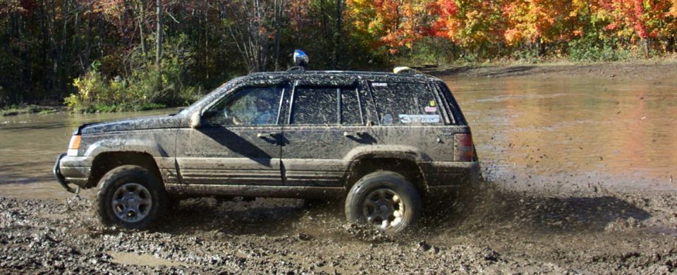 Muddy Jeep Grand Cherokee driving through a shallow water crossing with fall foliage in the background