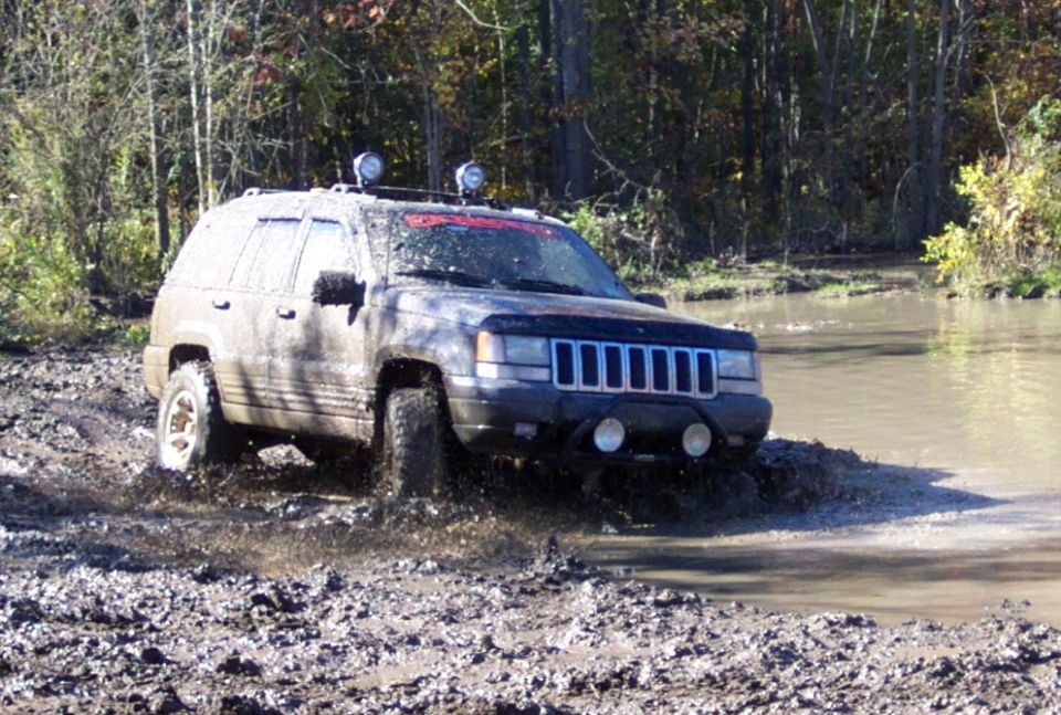 Muddy Jeep Grand Cherokee driving through water and mud on a wooded trail