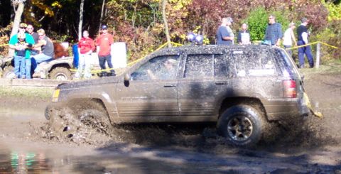 1979 Ford Bronco - A Jeep Grand Cherokee navigates a challenging muddy course with spectators watching.