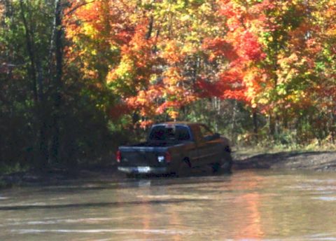 1979 Ford Bronco - A pickup truck navigates through a muddy area surrounded by trees with colorful autumn leaves.