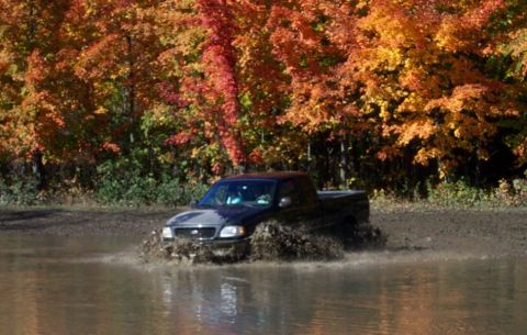 1979 Ford Bronco - A black pickup truck navigates a muddy puddle amidst autumn foliage.
