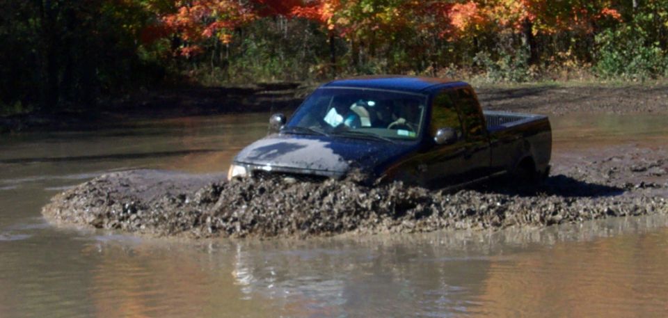 Black pickup truck stuck in deep mud and water, with fall foliage in the background