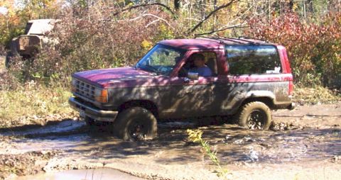 1979 Ford Bronco - A red SUV is stuck in a muddy trail during an off-road excursion.