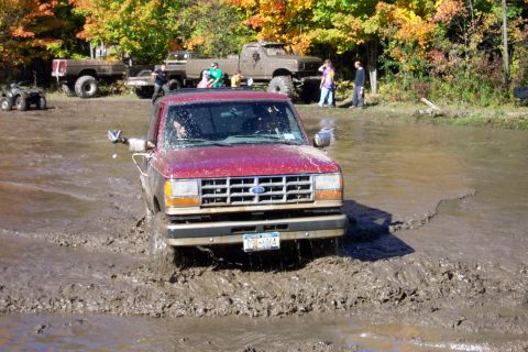 1979 Ford Bronco - A red 1989 Ford Ranger navigates a muddy obstacle course, with other trucks and ATVs visible in the background.