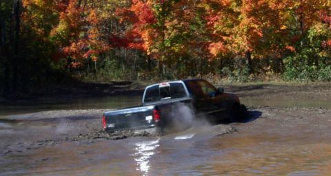 1979 Ford Bronco - A black pickup truck is stuck in the mud during autumn, with colorful trees visible.