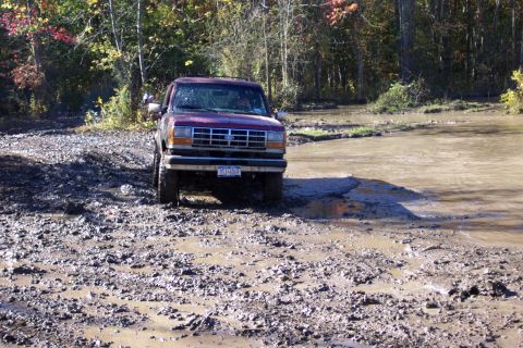 1979 Ford Bronco - A maroon Ford Explorer navigates a muddy terrain with water obstacles.