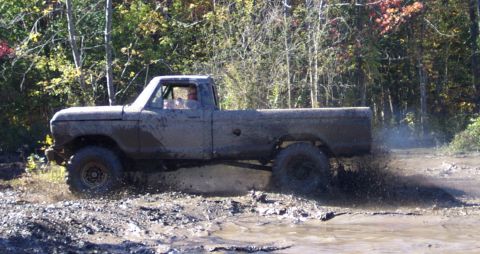 1979 Ford Bronco - This pickup truck is kicking up a lot of mud as it drives through a wet, wooded area.