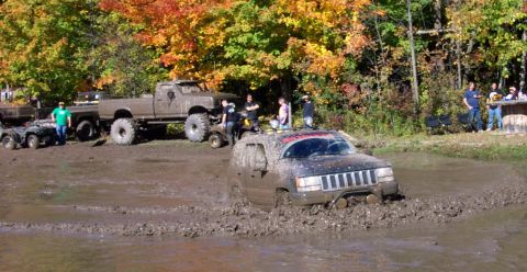 1979 Ford Bronco - A Jeep Grand Cherokee is stuck in the mud during an off-road event with other vehicles and spectators present.