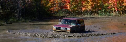 1979 Ford Bronco - A red 1989 Ford Bronco navigates a muddy trail during autumn.