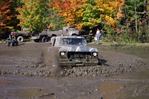 1979 Ford Bronco - A muddy pickup truck navigates a challenging mud pit with other vehicles and spectators in the background.