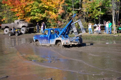 1979 Ford Bronco - A blue tow truck is stuck in a muddy area during an off-road event with spectators in the background.