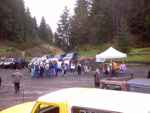 1976 Ford F-100 - Several vehicles and people gathered in a parking lot near a wooded area, with a white canopy set up.