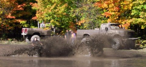 1979 Ford Bronco - Two trucks are seen mud bogging with people watching in the background.