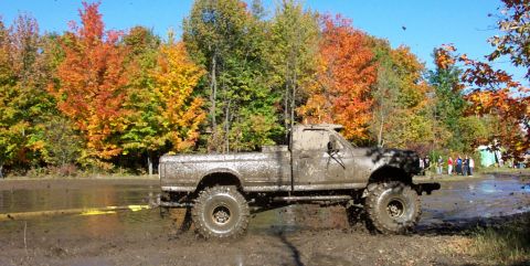 1979 Ford Bronco - A heavily mud-splattered pickup truck navigates a challenging off-road course amidst vibrant autumn trees.