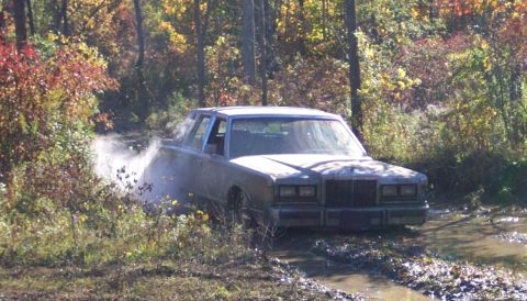 1979 Ford Bronco - A silver sedan navigates a muddy trail surrounded by autumn foliage.
