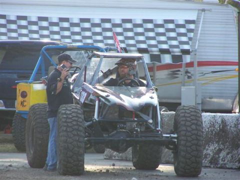 1995 Ford Bronco - Two custom off-road vehicles are parked at an event, with a person holding a camera near one of them.