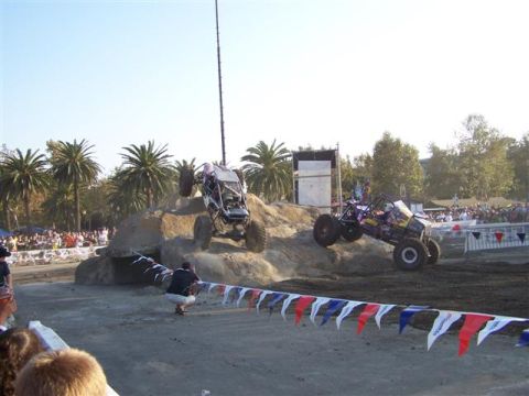 1995 Ford Bronco - Two off-road buggies compete on a dirt course with spectators watching in the background.