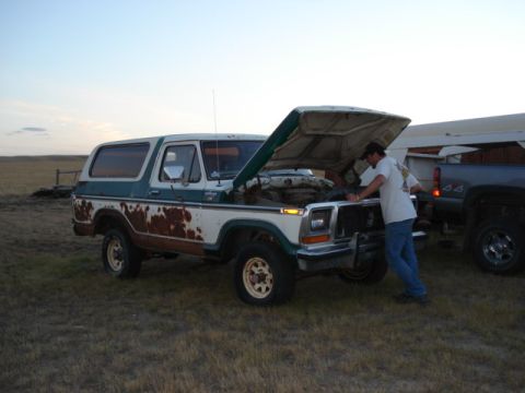 1979 Ford Bronco - Man works on the engine of a weathered Ford Bronco. A second truck is visible in the background.