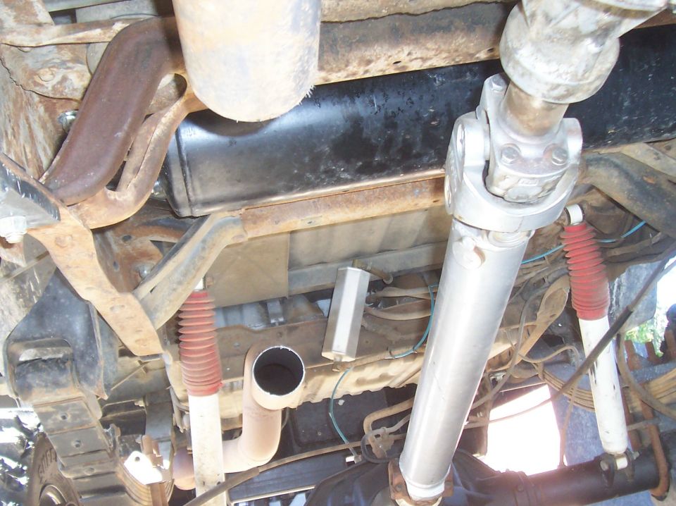 Undercarriage view of truck exhaust pipes, muffler, driveshaft, and red-booted shocks