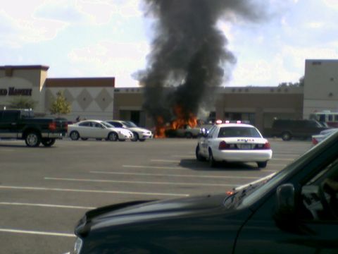 1995 Ford Bronco - A car is engulfed in flames in a parking lot, with a police car on the scene.