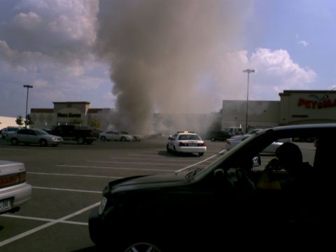 1995 Ford Bronco - A large plume of smoke billows into the sky from behind a shopping center, with a police car in the foreground.