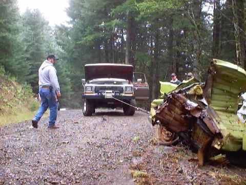 1976 Ford F-100 - A Ford Bronco is being towed by another truck in a wooded area, with a wrecked vehicle nearby.