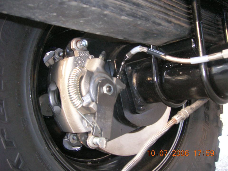 Rear disc brake caliper and rotor on black axle with braided brake line and e-brake cable
