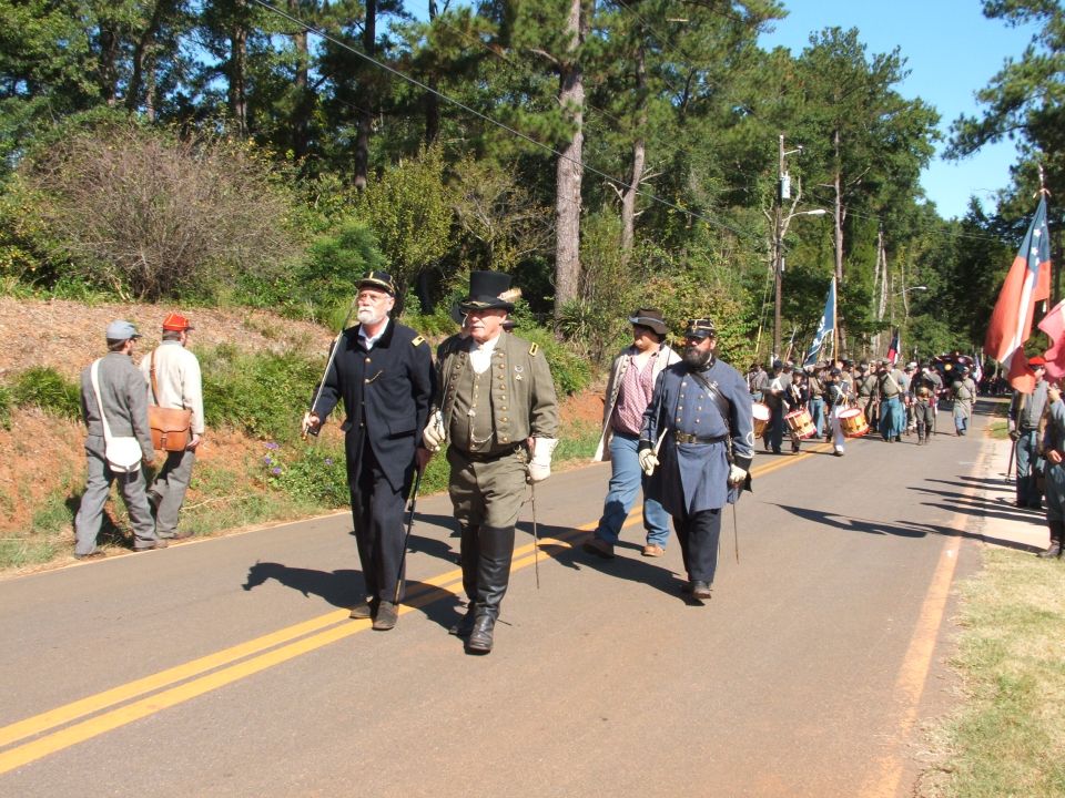 Civil War reenactors marching in a parade, some carrying flags and drums