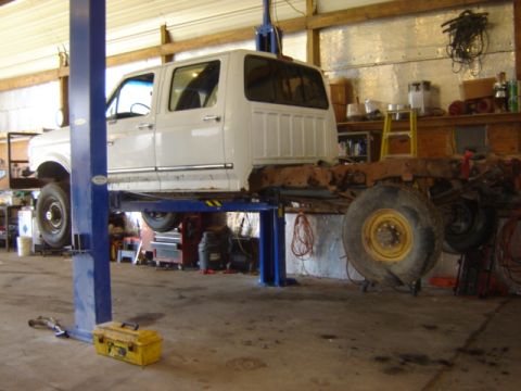 1992 Ford Bronco - A white crew cab truck is raised on a lift in a garage, revealing its chassis and suspension components.