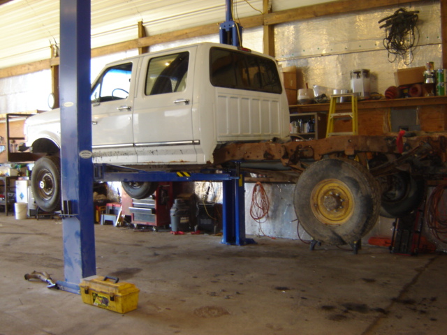 White crew cab truck body on a lift, chassis exposed