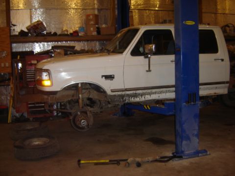 1992 Ford Bronco - A white 1992 Ford Bronco is undergoing maintenance in a workshop, with its front wheel detached.