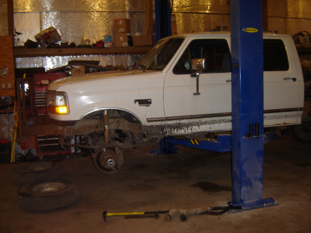 White 1992 Ford Bronco on a lift, front wheel removed, in a garage