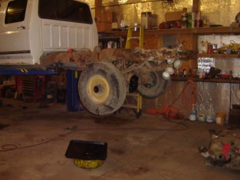 1992 Ford Bronco - Truck chassis undergoing work in a garage, with tools and shelves visible in the background.
