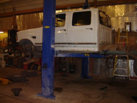 1992 Ford Bronco - A white crew cab truck is elevated on a hydraulic lift inside a workshop.