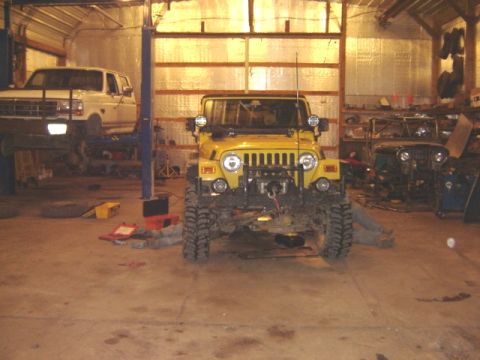 1992 Ford Bronco - Yellow Jeep Wrangler and white Ford truck inside a garage with repair equipment.
