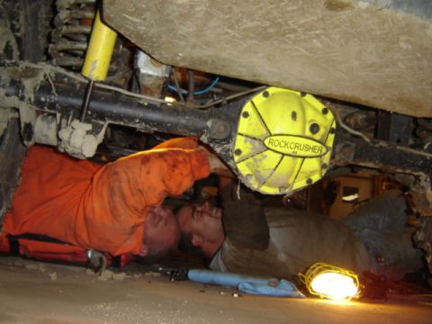 1992 Ford Bronco - Two mechanics are working on the undercarriage of a vehicle, with a yellow differential cover visible.