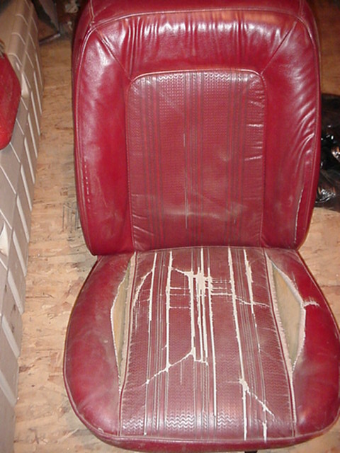 1979 Ford Bronco - A worn red car seat with significant damage to the seat cushion.