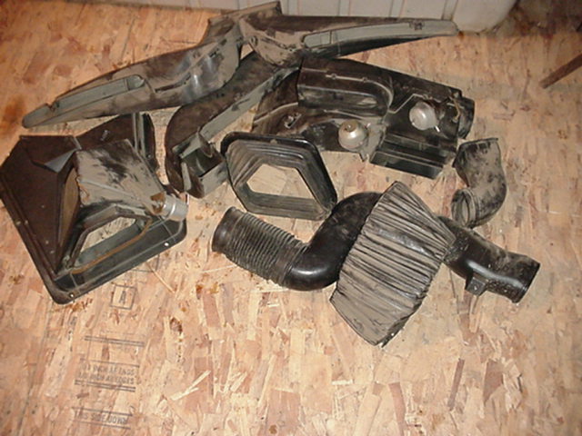 Pile of black plastic and rubber automotive HVAC ducting components on a plywood surface