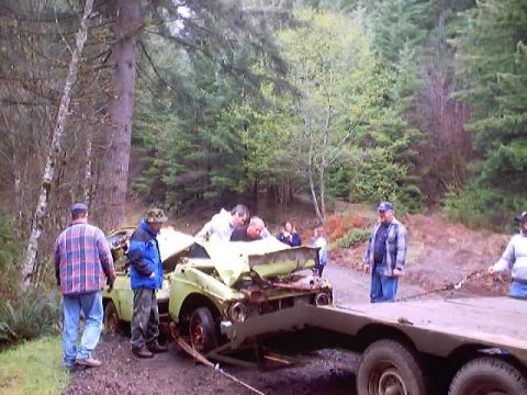 1976 Ford F-100 - A severely damaged sedan is being winched onto a trailer in a forest setting.