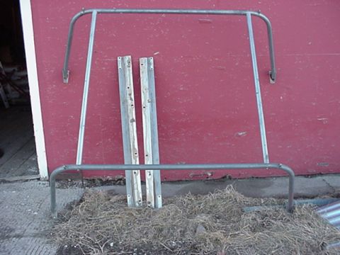 1979 Ford Bronco - A roll cage and two metal mounting brackets are shown leaning against a red wall.